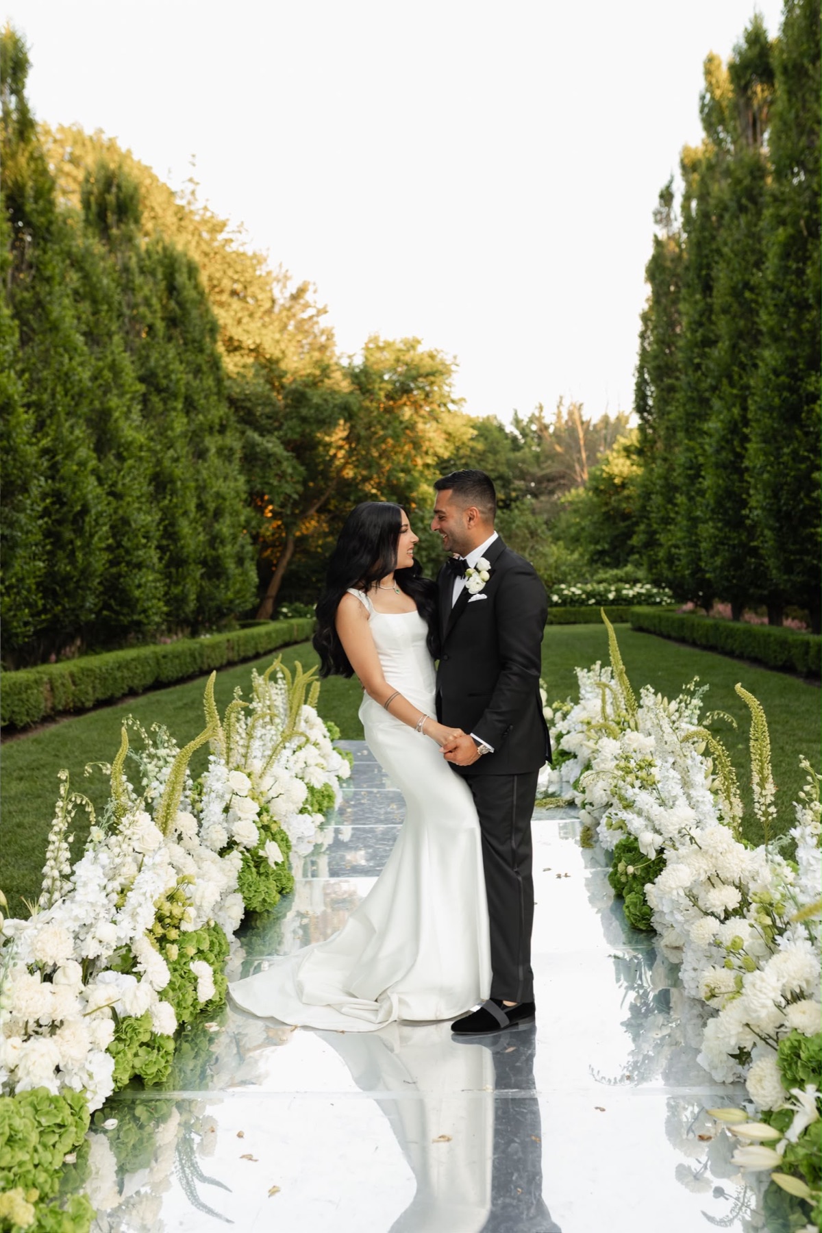 A couple together on a mirrored aisle framed by white and green flowers
